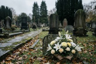 Arrangements floraux blancs déposés sur une tombe en pierre dans un cimetière automnal, avec des feuilles mortes et des cyprès en arrière-plan